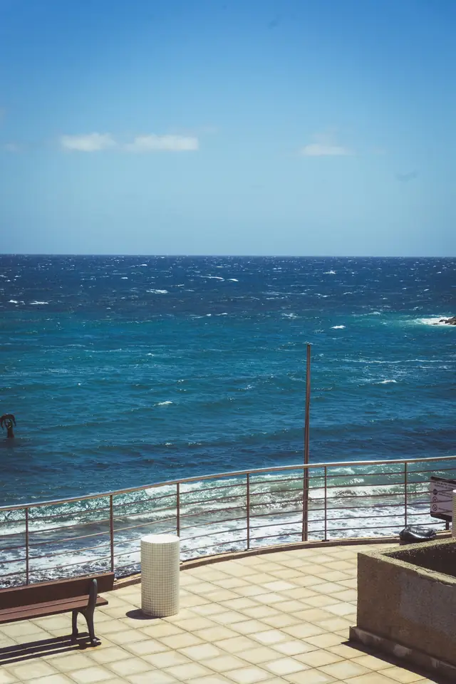 Terrasse carrelée face à une mer agitée par le vent, garde-corps et banc